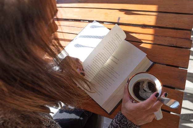 Donna irriconoscibile che legge un libro e beve un caffè all'aperto