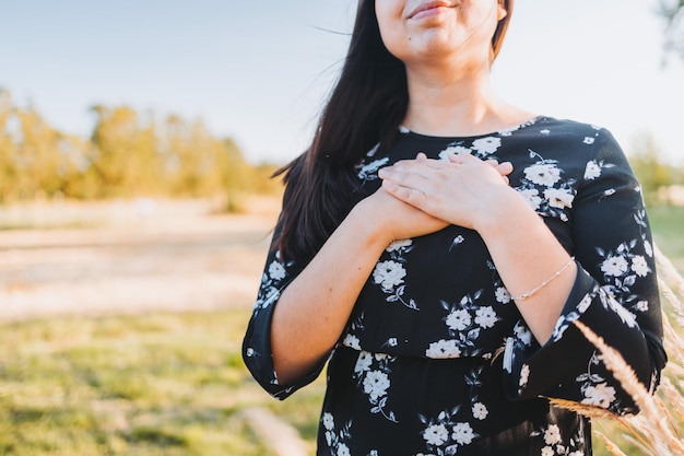 Donna irriconoscibile che mette le mani sul cuore in segno di gratitudine per le benedizioni di Dio, nel campo.