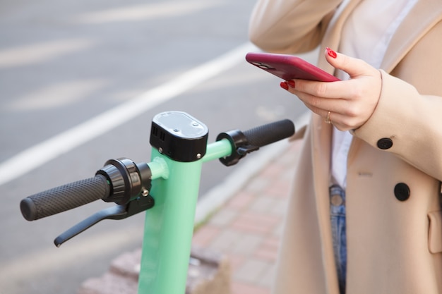 Donna irriconoscibile che utilizza l'app mobile sul suo smartphone per noleggiare uno scooter elettrico