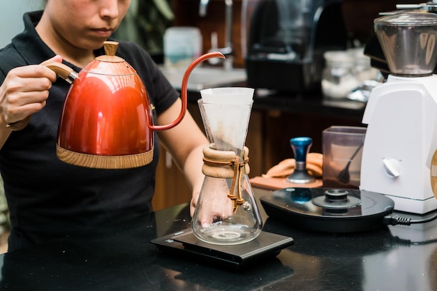 Donna irriconoscibile che versa acqua per preparare il caffè al lavoro. Copia spazio.