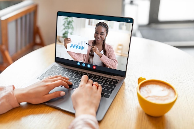 Donna irriconoscibile di affari online che fa teleconferenza con il collega mentre è seduto nella caffetteria