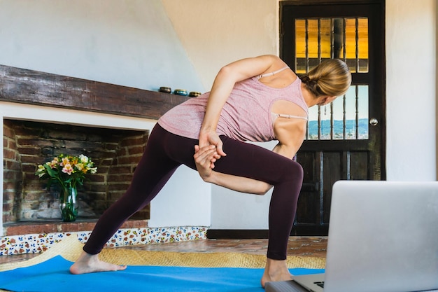 Donna irriconoscibile in appartamento che esegue una posa flessibile per la lezione di yoga online. Benessere mentale.