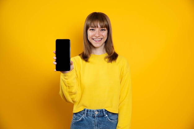 Donna isolata su uno sfondo giallo che mostra il telefono cellulare con schermo vuoto