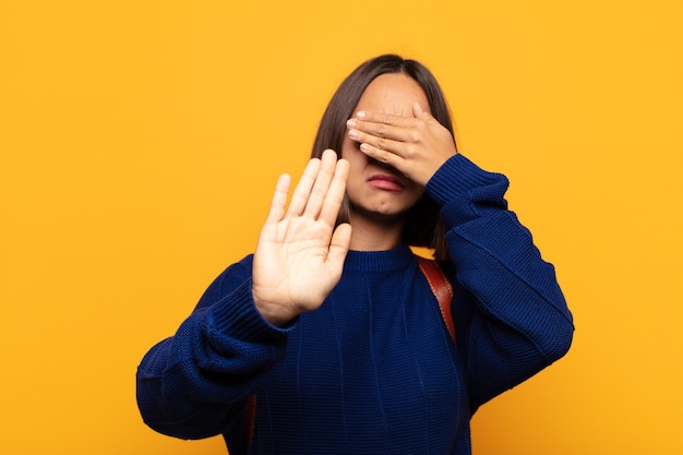 Donna ispanica che copre il viso con la mano e mette l'altra mano davanti per fermare la fotocamera, rifiutando foto o immagini