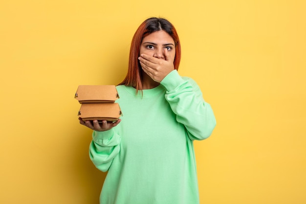 Donna ispanica che copre la bocca con le mani con uno scioccato. concetto di hamburger da asporto