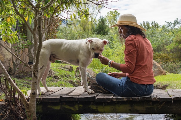 Donna ispanica che indossa un cappello seduto su un vecchio ponte di legno con cane bianco