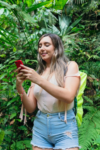 Donna ispanica che scrive un messaggio con il cellulare in una foresta tropicale