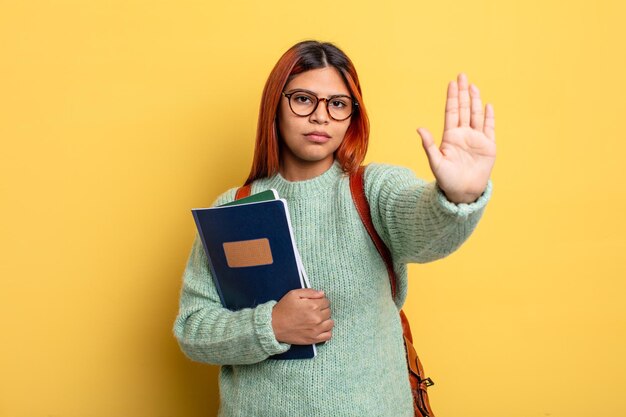 Donna ispanica che sembra seria mostrando il palmo aperto che fa il gesto di arresto. concetto di studente