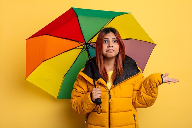Donna ispanica che si sente perplessa, confusa e dubita. concetto di pioggia e ombrello