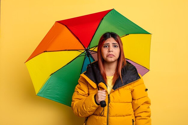 Donna ispanica che si sente triste e piagnucolona con uno sguardo infelice e piange. concetto di pioggia e ombrello