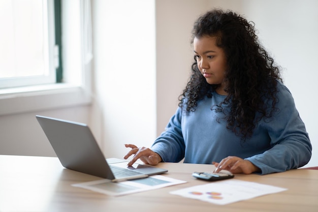 Donna ispanica concentrata che lavora da casa utilizzando lo spazio della copia del laptop