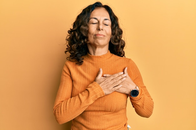 Donna ispanica di mezza età che indossa abiti casual sorridenti con le mani sul petto con gli occhi chiusi e gesto grato sul viso. concetto di salute.