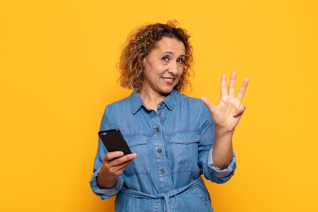 Donna ispanica di mezza età che sorride e sembra amichevole, mostrando il numero quattro o quarto con la mano in avanti, contando alla rovescia