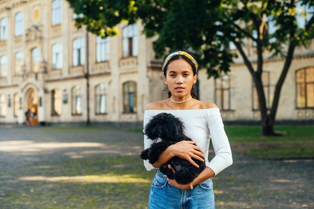 donna ispanica in piedi con un simpatico cane in braccio su uno sfondo di una bellissima vista urbana