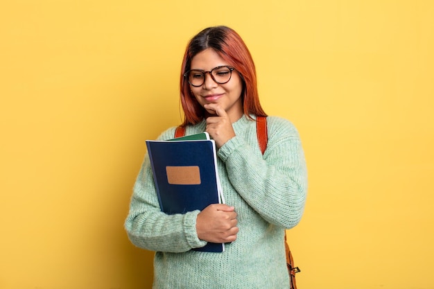 Donna ispanica sorridente con un'espressione felice e sicura con la mano sul concetto di studente mento