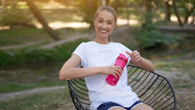 Donna itting sedia bere acqua bottiglia rossa dopo l'allenamento mattutino.