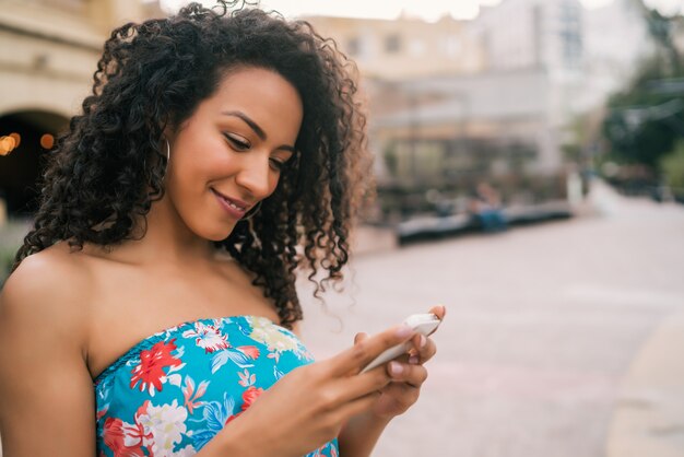 Donna latina afroamericana che per mezzo del telefono cellulare.