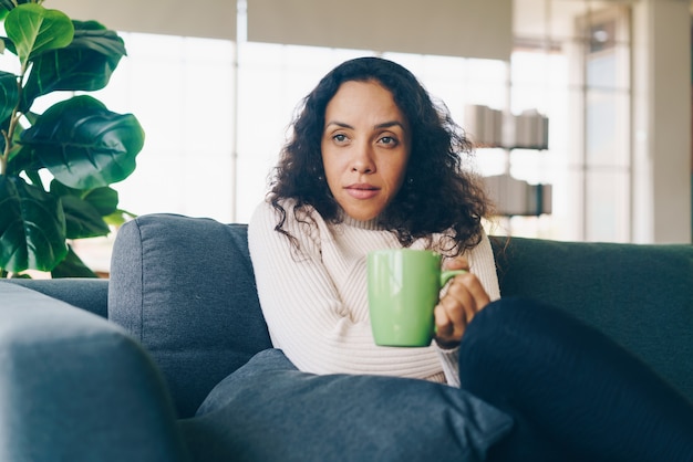 Donna latina che beve caffè sul divano di casa