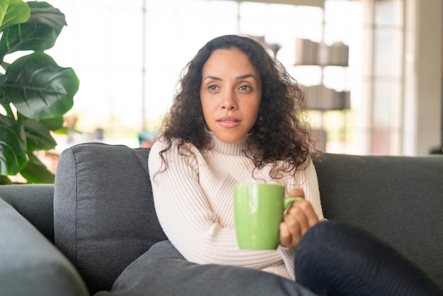 Donna latina che beve caffè sul divano di casa