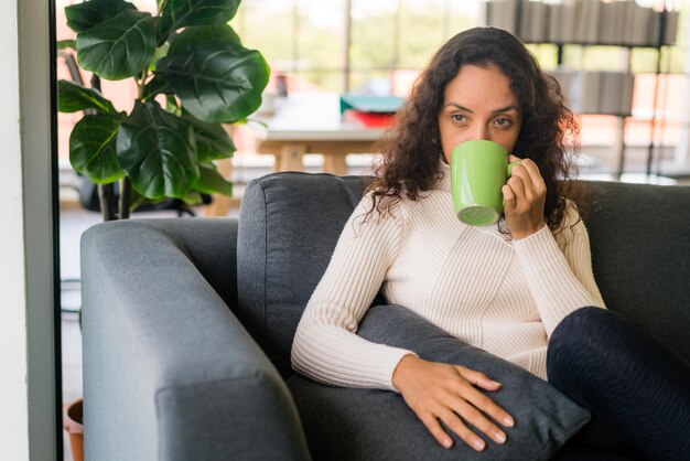 Donna latina che beve caffè sul divano di casa