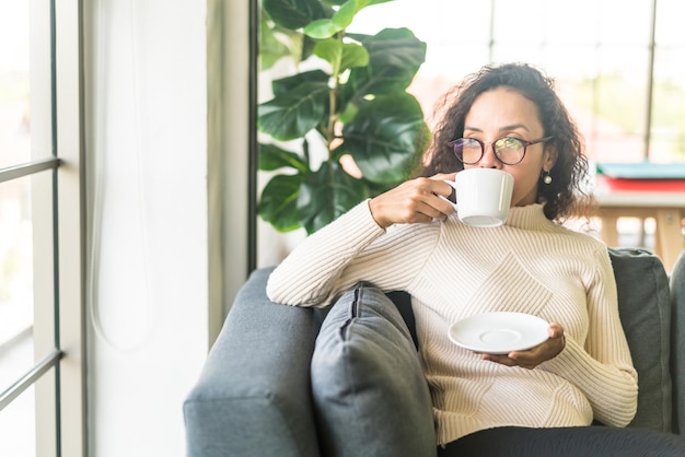 Donna latina che beve caffè sul divano di casa