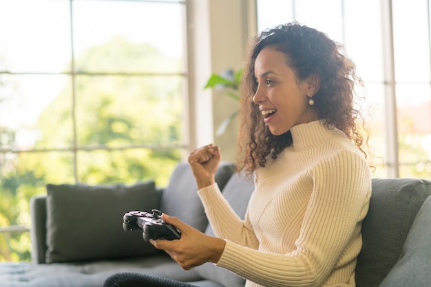 Donna latina che gioca ai videogiochi con le mani che tengono il joystick sul divano di casa