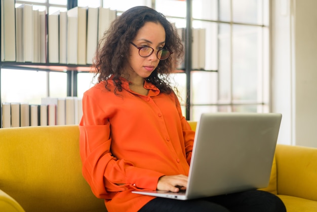 donna latina che lavora con il computer portatile sul divano di casa