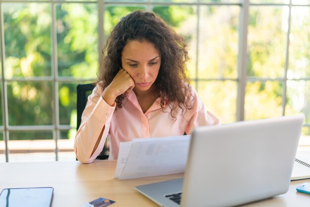 Donna latina che lavora con laptop e carta sullo spazio di lavoro a casa