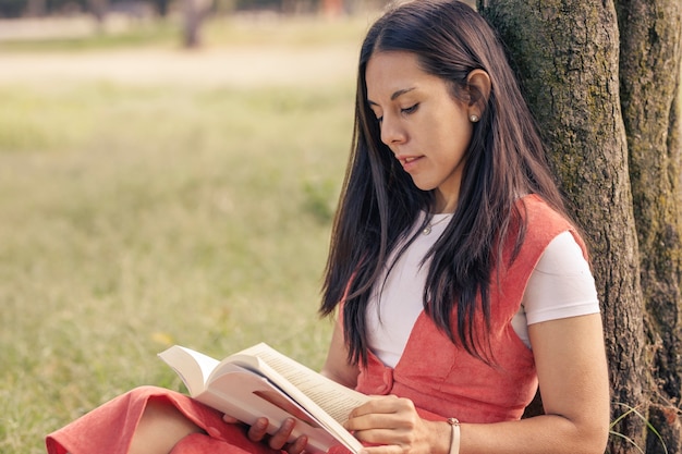 Donna latina che legge un libro decorato di un albero nel parco