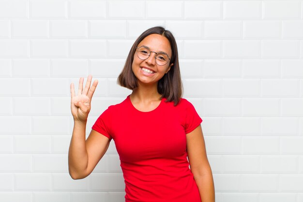 Donna latina che sorride e sembra amichevole, mostrando il numero quattro o quarto con la mano in avanti, contando alla rovescia