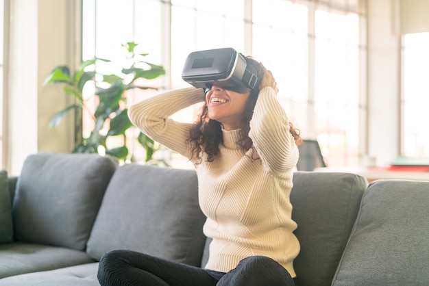 Donna latina che utilizza un auricolare per realtà virtuale sul divano di casa