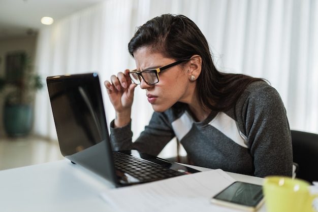 Donna latina con problemi di vista che prova a leggere contenuti online su un laptop