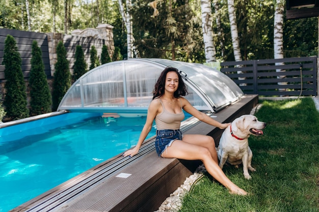 Donna latina da una piscina con un cane da riporto al ritratto del tramonto