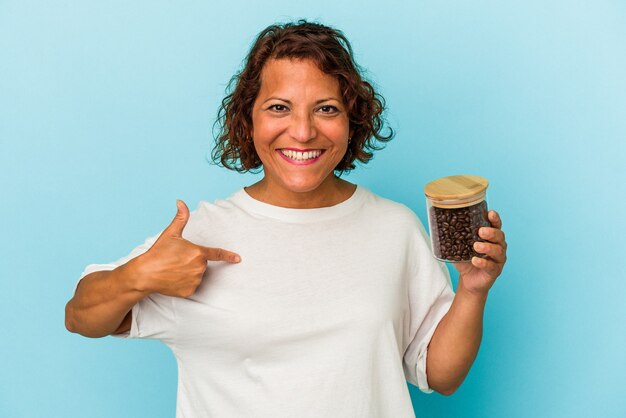 Donna latina di mezza età che tiene un barattolo di caffè isolato su sfondo blu persona che punta a mano a uno spazio copia camicia, orgoglioso e fiducioso