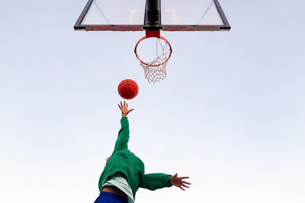 Donna latina irriconoscibile che spara in un canestro da basket visto dal basso con il cielo sullo sfondo il concetto di sport urbano all'aperto copia spazio per il testo