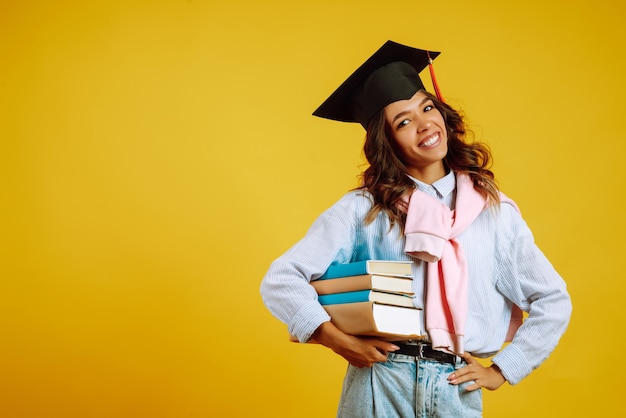 Donna laureata in un cappello di laurea in testa, con libri su giallo.