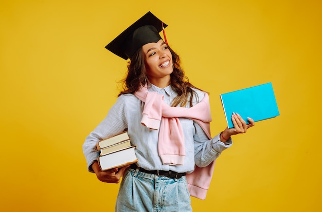 Donna laureata in un cappello di laurea in testa, con libri su giallo.