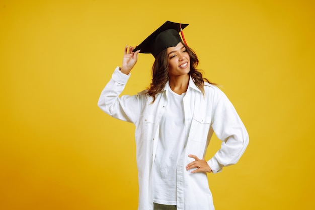 Donna laureata in un cappello di laurea sulla sua testa in posa sul giallo