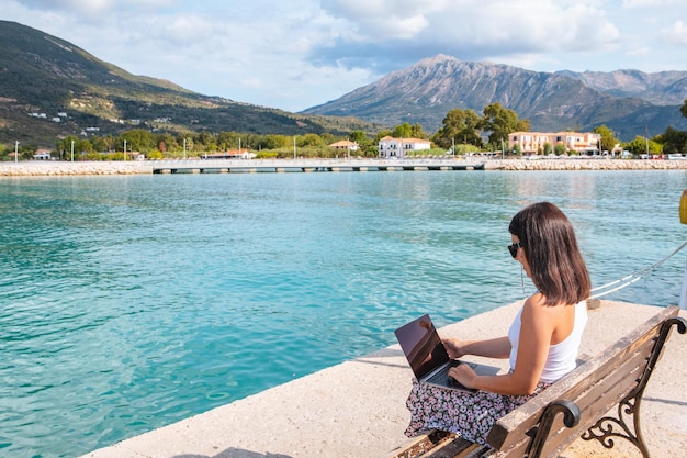 Donna libera professionista sorridente che lavora al computer portatile all'aperto nello spazio della copia del porto della città