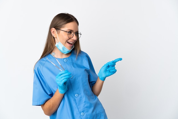 Donna lituana dentista tenendo gli strumenti su sfondo isolato puntando il dito a lato e presentando un prodotto