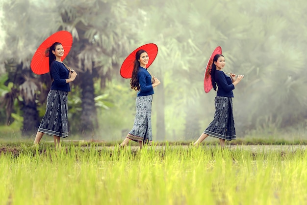 Donna locale asiatica che sta con l'ombrello rosso nell'azienda agricola del riso, Sakonnakhon, Tailandia