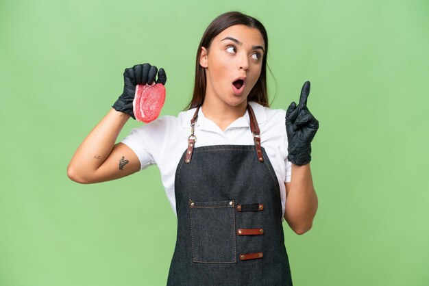 Donna macellaio che indossa un grembiule e serve carne fresca tagliata isolata su sfondo verde croma pensando a un'idea che punta il dito verso l'alto