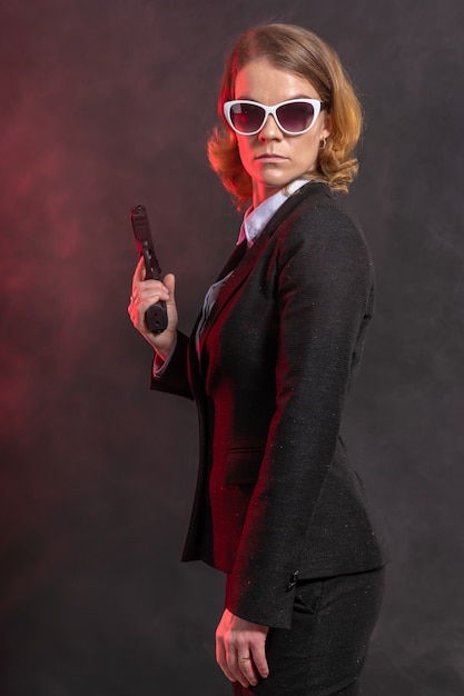 Donna mafiosa con una pistola in mano. ritratto su una parete scura con luce rossa.