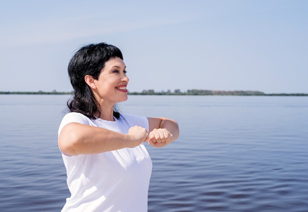 Donna maggiore attiva e felice che si esercita vicino alla riva del fiume