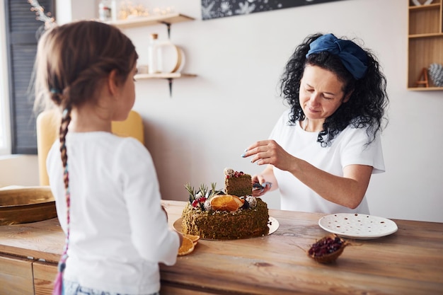 Donna maggiore con sua nipote che mangia una torta dietetica fresca in cucina