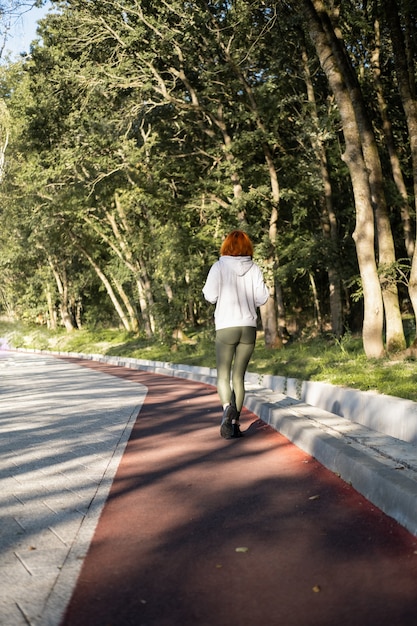 Donna magra allo zenzero in abiti sportivi che corre nel parco il mattino sano stile di vita fitness