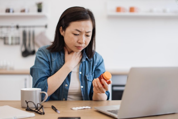 Donna malata con mal di gola che tiene in mano delle pillole durante una conversazione online