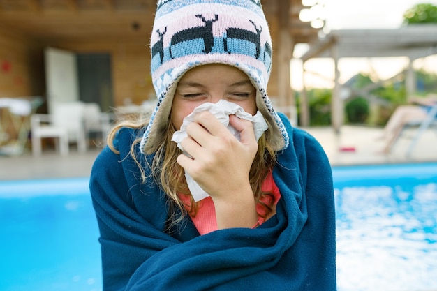 Donna malata dell'adolescente che si siede nel cappello caldo sotto la coperta con il tovagliolo