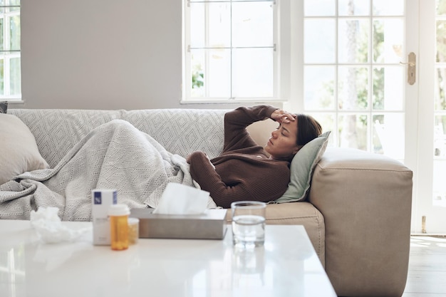 Donna malata e mal di testa con farmaci sul divano per il raffreddore o il sinus nel soggiorno a casa Persona femminile stanca con malattia febbre o influenza in stanchezza o addormentata sul divano da paracetamolo