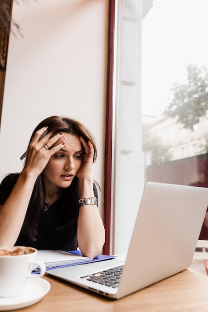 Donna manager con forte mal di testa che lavora su un laptop online da remoto in un bar loft La ragazza triste con il laptop ha avuto l'emicrania che le tocca la testa a causa del dolore